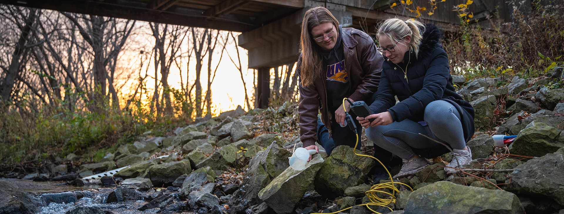 Photo of two undergraduate students using a digital probe to collect real-time water data from Dry Run Creek in Black Hawk County.